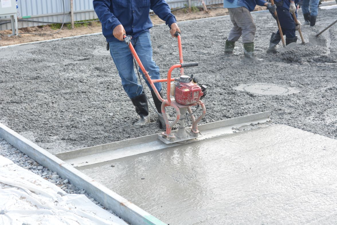 Concrete workers leveling a freshly poured slab with power tools at a building site.