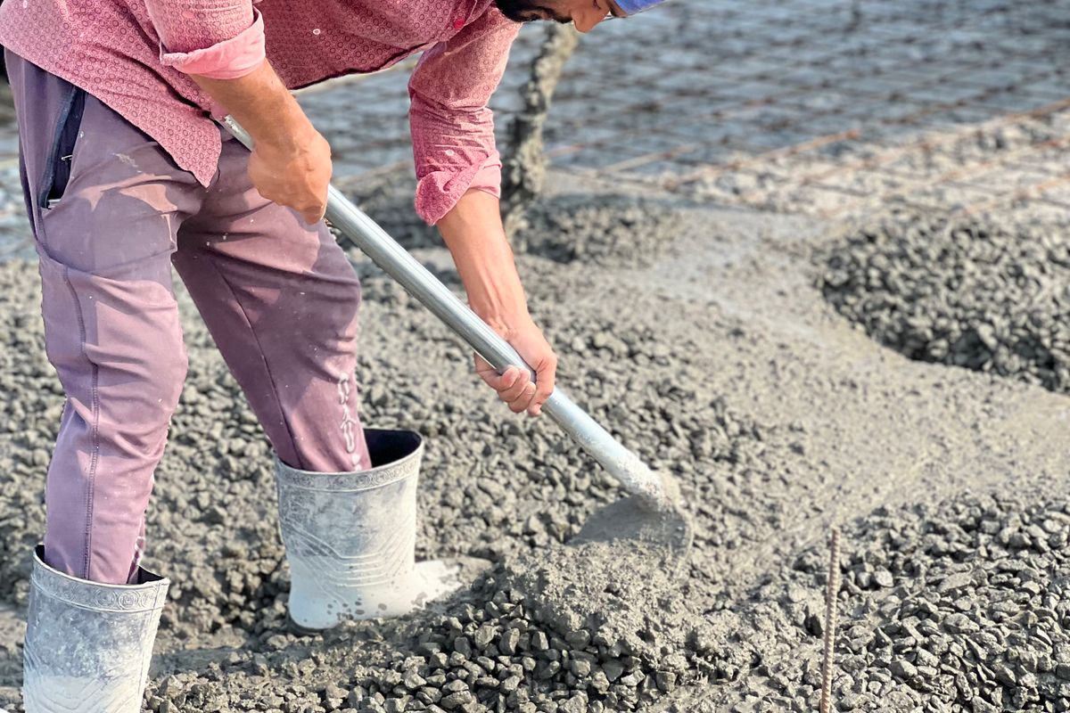 Worker spreading fresh concrete with a shovel during a slab repair pour.