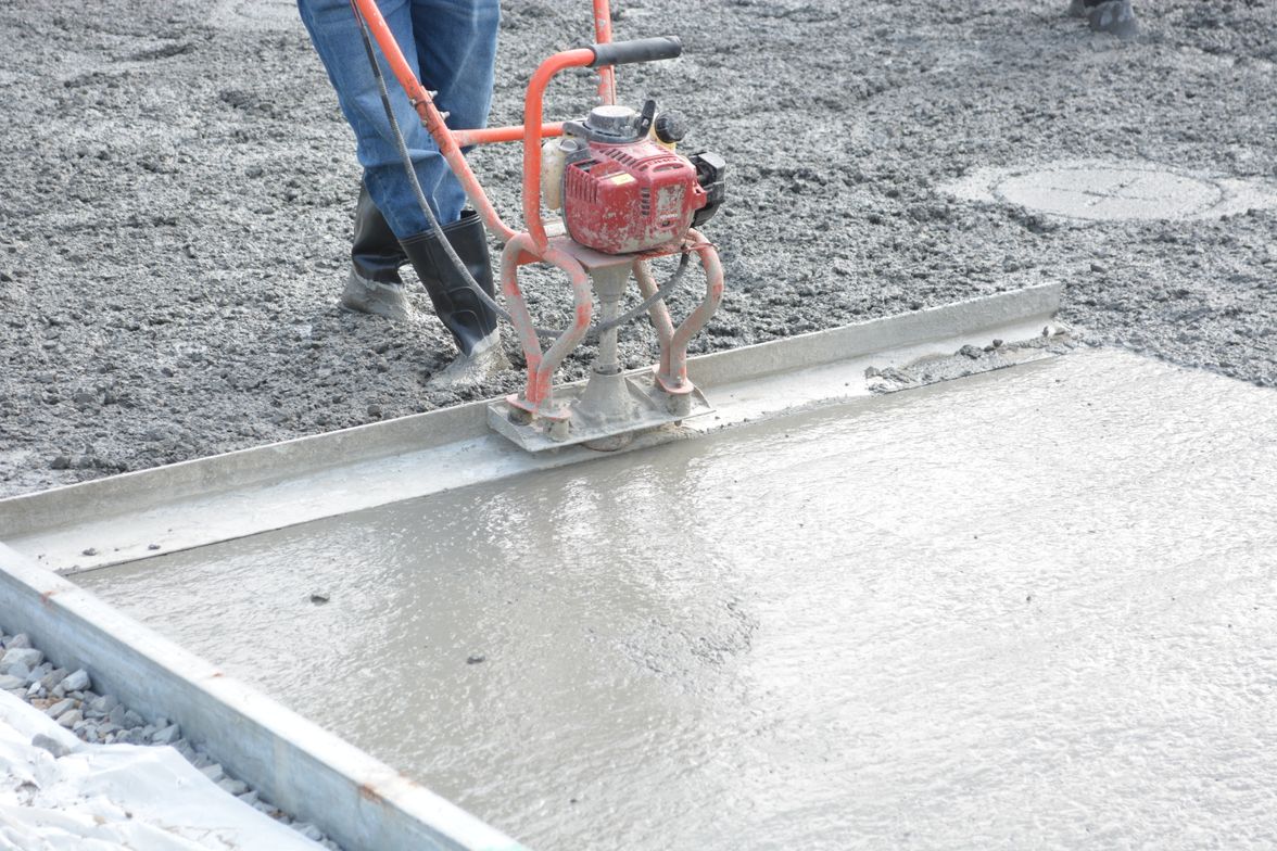 Operator running a power trowel across a curing concrete slab to finish the surface.